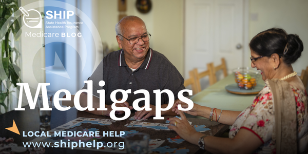 An older couple is sitting at a table and completing a jigsaw puzzle. The man is wearing glasses and a dark polo shirt, and the woman is wearing a floral sari and glasses.