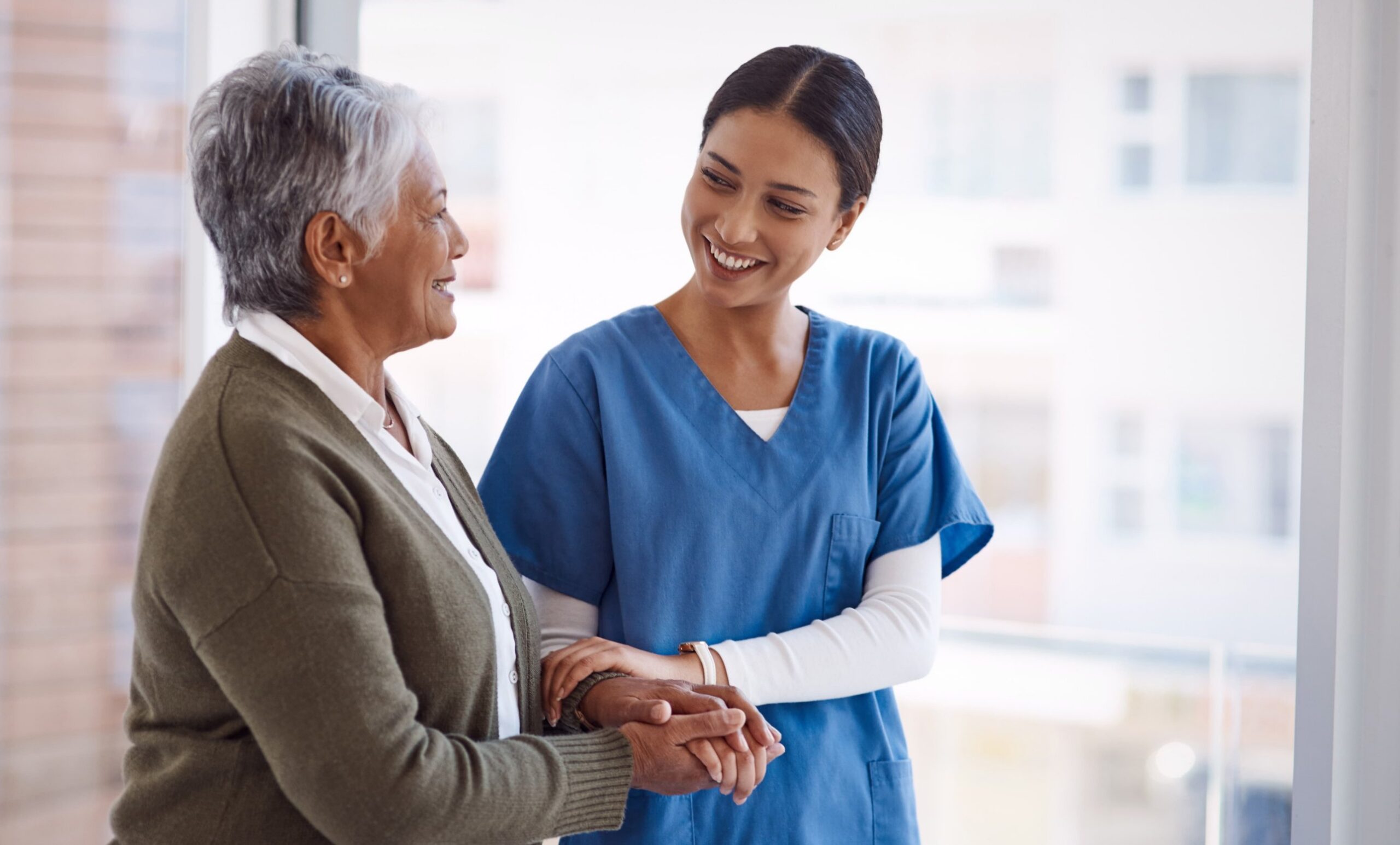 A smiling healthcare worker holding the hands of an older woman