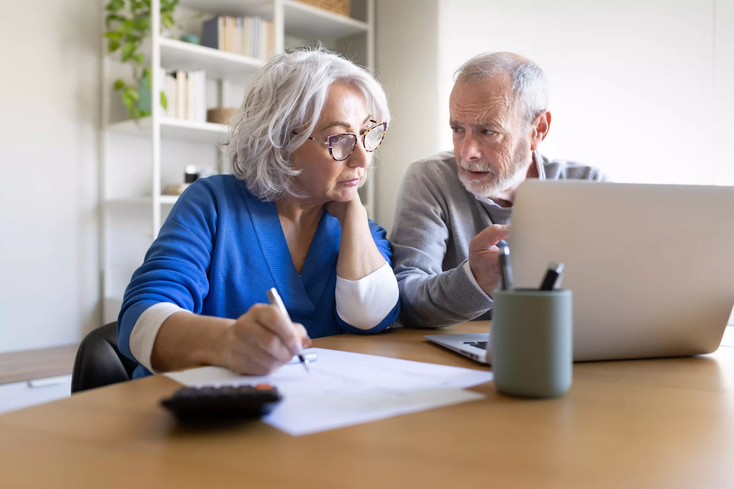 An older couple reviewing paperwork and a laptop together at a table
